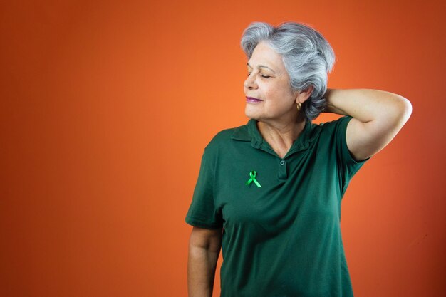 Dia mundial da saúde mental Mulher madura com fita verde de cabelo grisalho e camisa isolada em laranja