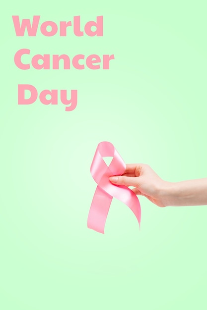 Foto dia mundial do câncer. a mão de uma mulher com uma fita rosa sobre um fundo verde claro. orientação vertical. copie o espaço.