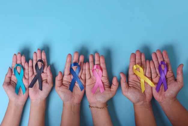 Dia Mundial do Câncer. Mãos de pessoas segurando fitas coloridas de conscientização para apoiar pessoas