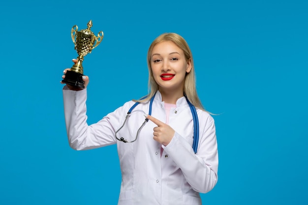 Día mundial del médico lindo joven médico con trofeo dorado y el estetoscopio en la bata médica