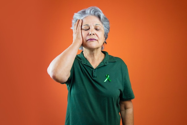 Día mundial de la salud mental Mujer madura con cabello gris cinta verde y camisa aislada en naranja