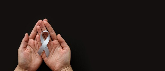 Foto día mundial del tumor cerebral las manos de la persona sostienen una cinta gris sobre fondo negro