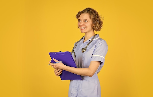 Dia normal de trabalho Médica sorridente com uma pasta de uniforme em pé Retrato de uma adorável enfermeira com uma pasta Ela está usando uma enfermeira de estetoscópio segurando fichário e usando estetoscópio