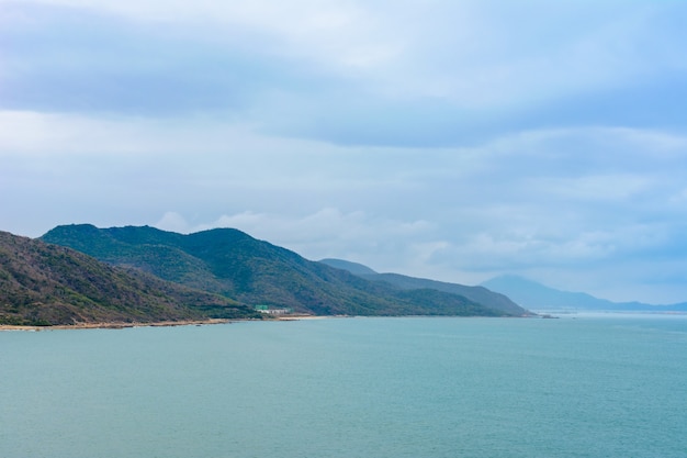 Día nublado, playa desierta de arena de la costa cerca de la estatua de la diosa Nanshan en el Mar de China Meridional. Sanya, isla de Hainan, China. Paisaje de la naturaleza.