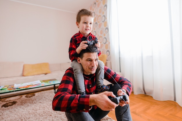 Día del padre y el hijo. Alegre padre e hijo jugando videojuegos. Hijo está sentado sobre los hombros del padre.
