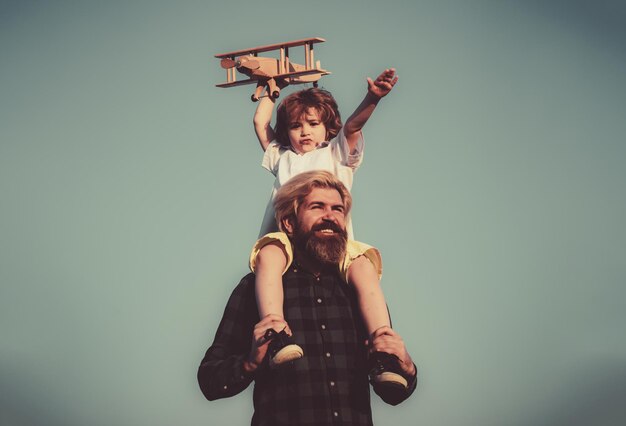 Día del padre Padre e hijo Padre dando a su hijo un paseo en la espalda Retrato de un padre feliz dando a su hijo un paseo a cuestas sobre sus hombros y mirando hacia arriba Chico lindo con papá jugando con un avión de madera al aire libre