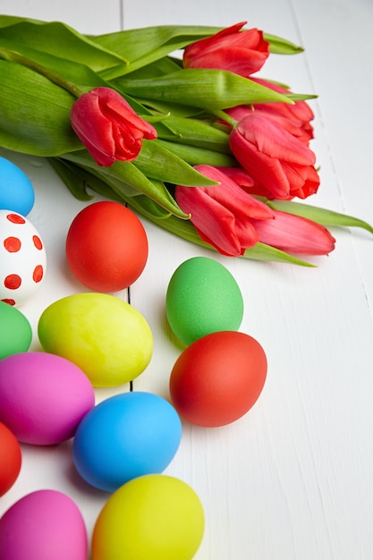 Día de Pascua coloridos huevos de gallina y flores de tulipán rojo sobre mesa de madera blanca
