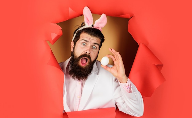 El día de pascua sorprendió a un hombre barbudo con huevo blanco mirando a través de huevos de papel cazando vacaciones de primavera