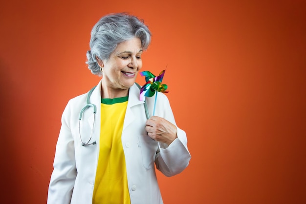 Día del pediatra Doctora madura con cabello gris y juguetes para niños aislados en fondo naranja