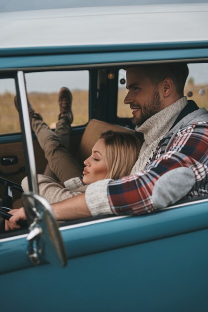 Dia perfeito juntos. Mulher jovem e atraente descansando nos braços do namorado enquanto viaja em uma minivan estilo retro