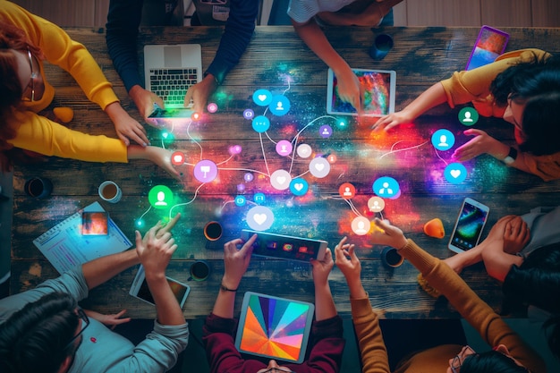 Foto día de las redes sociales un grupo de personas están sentadas alrededor de una mesa usando sus teléfonos y tabletas