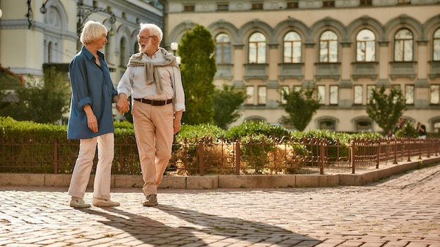 Día romántico hermosa y feliz pareja de ancianos tomados de la mano y hablando de algo mientras