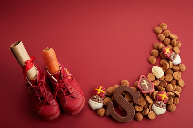 Día de san nicolás sinterklaas con zanahoria de zapatos y dulces tradicionales sobre fondo rojo.