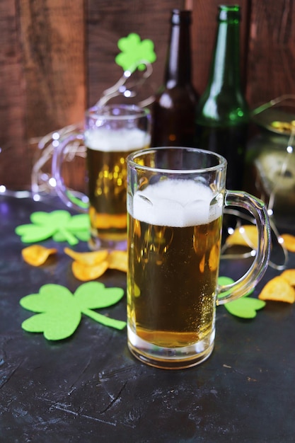 Día de San Patricio, cerveza espumosa en tazas de vidrio y una botella, papas fritas y galletas, tréboles verdes