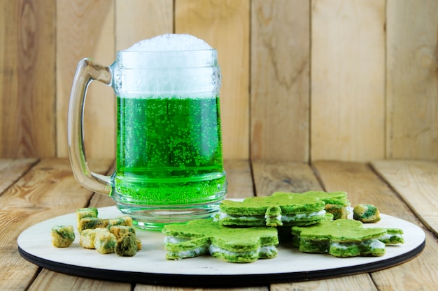 Día de San Patricio. Vaso verde de cerveza y aperitivos verdes en un tablero