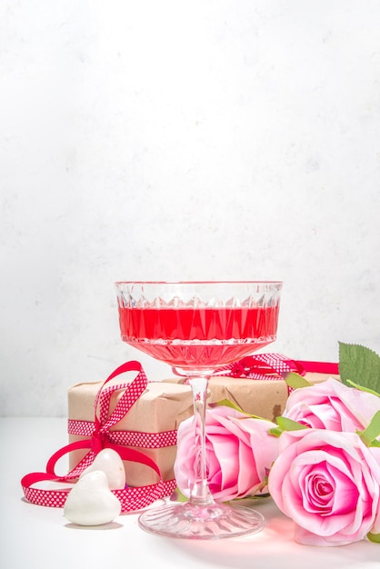 Día de San Valentín, 8 de marzo, fondo de tarjeta de felicitación del día de la madre. Ramo de flores de rosa rosa, caja de regalo artesanal con cinta roja, cóctel de vino de rosa en el espacio de copia de fondo de mesa blanca