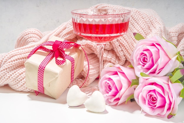 Día de San Valentín, 8 de marzo, fondo de tarjeta de felicitación del día de la madre. Ramo de flores de rosa rosa, caja de regalo artesanal con cinta roja, cóctel de vino de rosa en el espacio de copia de fondo de mesa blanca