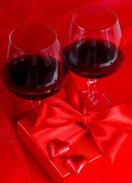 Día de San Valentín. Caja de regalo, flores, vasos con vino y dulces en forma de corazón sobre un fondo rojo.