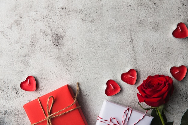 Día de San Valentín, caja de regalo de papel kraft con una cinta, rosa y velas sobre fondo gris