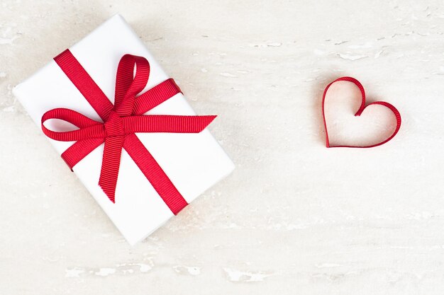 Día de San Valentín, concepto de cumpleaños con espacio para copiar. Corazón de cinta roja y caja de regalo sobre fondo claro