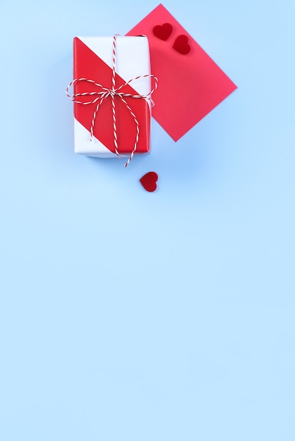 Día de San Valentín, concepto de diseño de arte del día de la madre para la promoción: caja de regalo envuelta en rojo, blanco aislada sobre fondo de color azul claro pastel, endecha plana, vista superior.