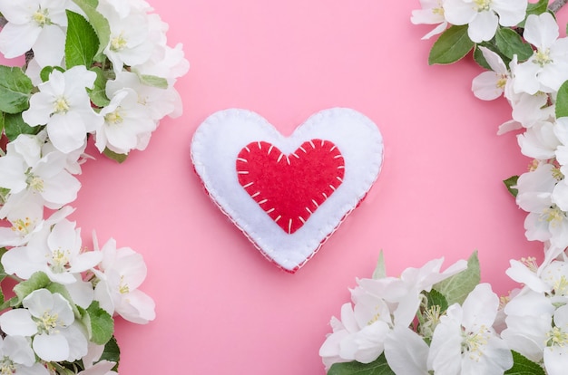 Día de San Valentín, corazón hecho a mano rojo y blanco con marco de flores de manzano sobre fondo rosa