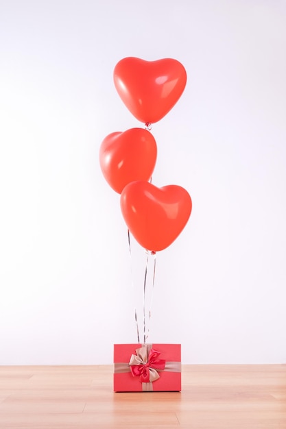 Día de San Valentín, Día de la Madre, concepto de diseño de cumpleaños - Globo de helio de corazón con caja de regalo en un suelo de madera clara, fondo de pared blanca, primer plano.