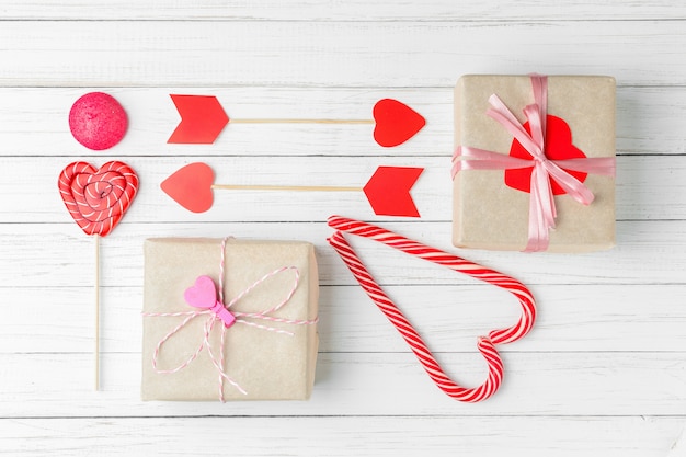 Día de San Valentín con dulces, caja de regalo y corazón cortado en papel sobre un fondo blanco de madera, vista superior en plano