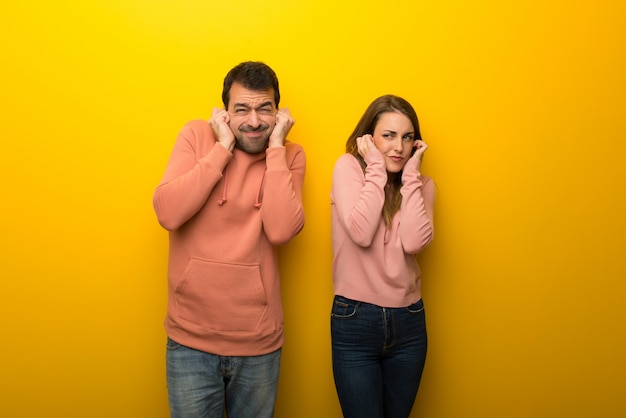 En el día de San Valentín Grupo de dos personas sobre fondo amarillo cubriendo las orejas con las manos. Expresion frustrada