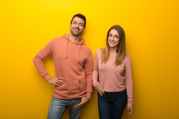 En el día de San Valentín Grupo de dos personas sobre fondo amarillo posando con los brazos en la cadera y sonriendo