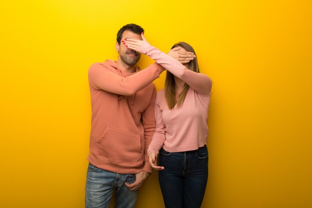 En el día de San Valentín Grupo de dos personas sobre fondo amarillo que cubre los ojos con las manos. Sorprendido de ver lo que está por delante.