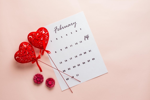 Día de San Valentín. Hoja de calendario con fecha destacada 14 de febrero y dos corazones en palos sobre un fondo rosa. Vista superior