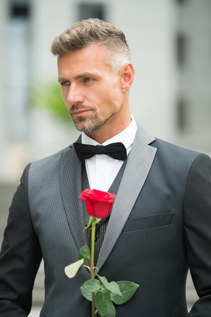 Día de San Valentín de hoy Chico guapo con regalo de flores de San Valentín el 14 de febrero Hombre elegante con flores frescas para la celebración del día de San Valentín San Valentín rojo rosa para simbolizar el amor verdadero