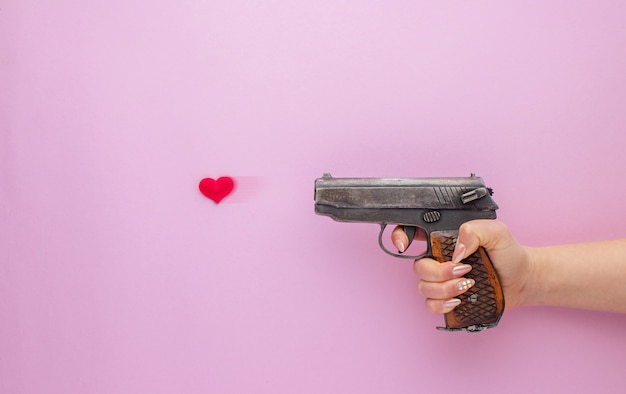 Día de San Valentín . Mano de mujer sosteniendo una pistola y disparando con corazón sobre fondo rosa.