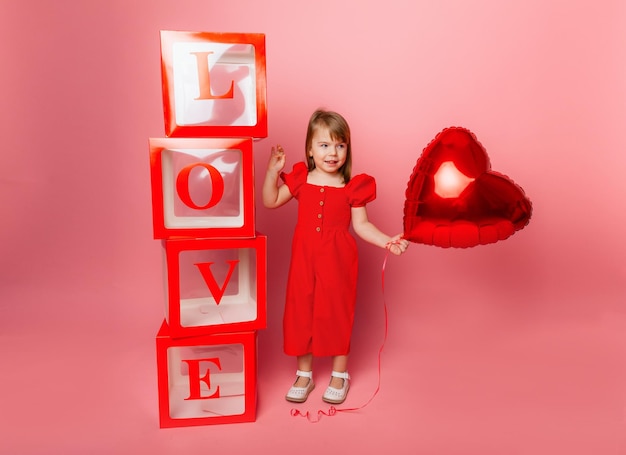 Día de San Valentín, Niña pequeña sosteniendo un gran globo en forma de corazón sobre un fondo rosa.