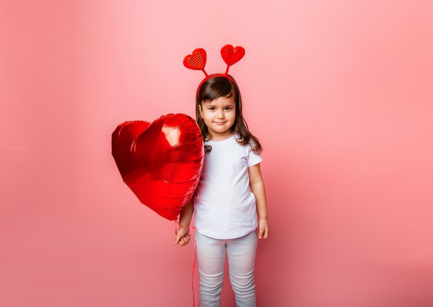 Día de San Valentín, Niña pequeña sosteniendo un gran globo en forma de corazón sobre un fondo rosa.