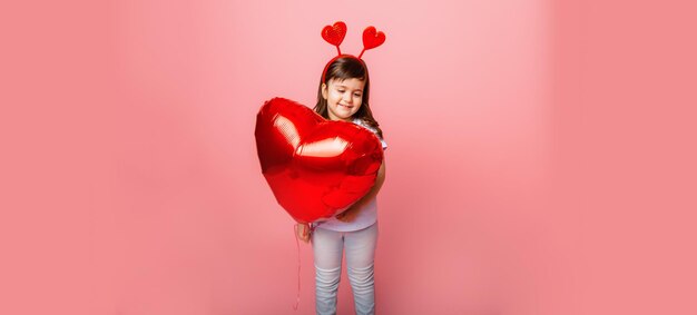 Día de San Valentín Niña sosteniendo un gran globo en forma de corazón sobre un fondo rosa