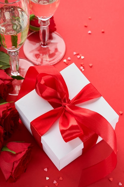Día de San Valentín o concepto de cena romántica Mesa romántica puesta cubiertos copas de vino caja de regalo rosas y símbolo de amor corazón rojo sobre fondo rojo Cena romántica Concepto de San Valentín