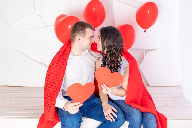 El día de San Valentín, una pareja enamorada tiene corazones rojos en sus manos y se miran con una mirada amorosa