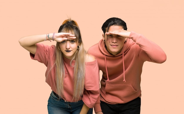 Foto en el día de san valentín pareja joven que mira lejos con la mano para mirar algo sobre fondo rosa