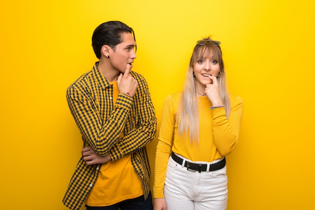 En el día de San Valentín Pareja joven sobre fondo amarillo vibrante que tiene dudas mientras mira hacia arriba