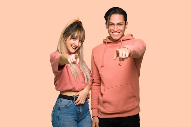 Foto en el día de san valentín, una pareja joven te señala con el dedo con una expresión de confianza sobre un fondo rosa.