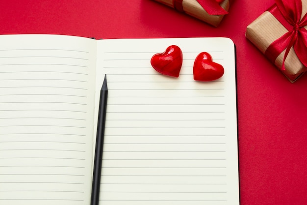 Día de San Valentín simulacro. Abra el cuaderno con corazones rojos y cajas de regalo, sobre fondo rojo, copie el espacio para el texto.