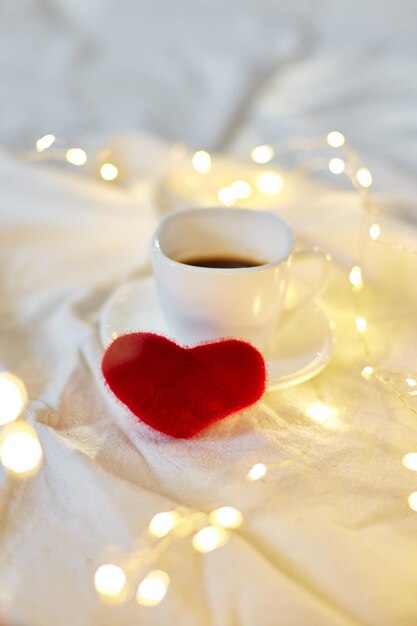 Foto día de san valentín taza de café en la cama con corazones rojos y luces copia espacio tarjeta de felicitación desayuno romántico