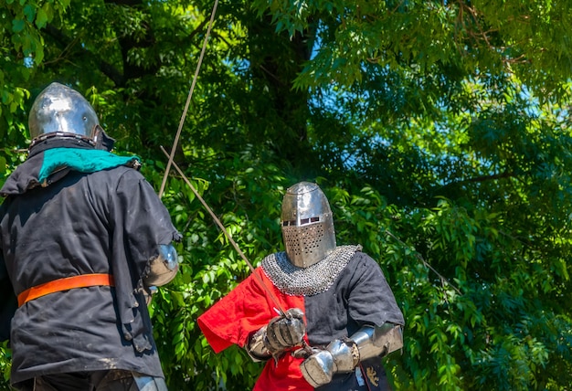 Día soleado de verano. Dos soldados medievales con armaduras y cascos de hierro luchando con espadas