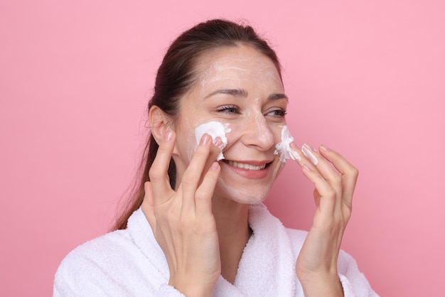 Día de spa Mujer hermosa aplicando una máscara en su cara sobre un fondo rosa
