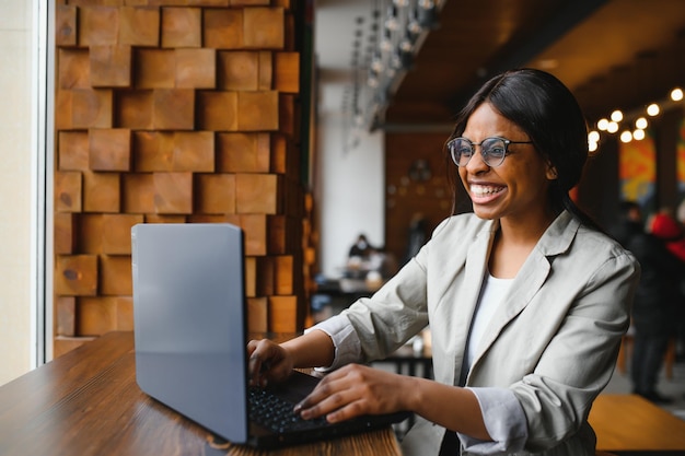 Día de suerte Mujer negra emocional mirando la computadora portátil apretando los puños y gritando trabajando en el espacio de copia del café