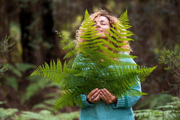 El día de la tierra y el concepto de amor por la naturaleza con una mujer hermosa con los ojos cerrados, sienta la hoja grande y disfrute de la actividad de ocio natural al aire libre