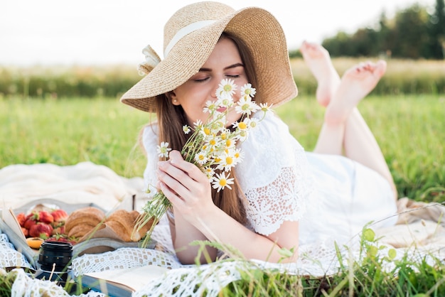 Día de verano, picnic en el pueblo. Una hermosa niña con un sombrero se encuentra en una tela escocesa. un ramo de margaritas, flores en el pelo.