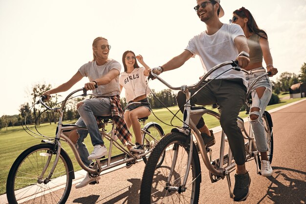 Día de verano sin preocupaciones. Grupo de jóvenes felices en ropa casual sonriendo mientras andan en bicicleta juntos al aire libre